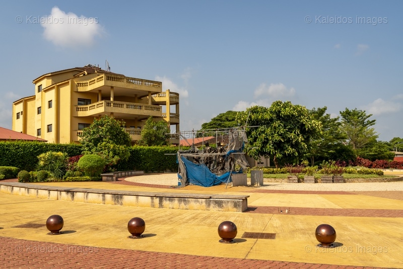 Place des Enchères Ouidah ; Place Chacha slave market Benin ; bronze sculptures slave trade ; spheres ground memorial Ouidah ; monumental heads Xweda Fon Yoruba ; memorial public art West Africa ; night lighting Ouidah square ; red laterite ground ; de Souza house Singbomey ; Afro-Brazilian heritage Ouidah ; Benin Revealed program