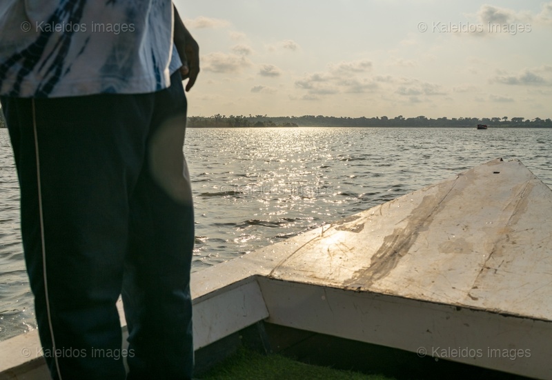 Lake Toho;Ouidah;Benin;West Africa;boat;golden hour;sunset;light reflection;sparkling water;man on boat;bow;lake crossing;contemplation;backlight;travel;Tarek Charara;Kaleidos;Kaleidos images;La parole à l'image