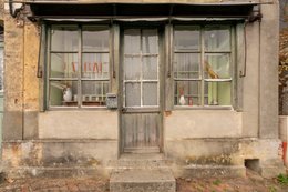 Architectural-heritage;-Calvados;-Ceramic-pitcher;-Derelict-facade;-Dereliction;-Detail;-Dried-flowers;-Faded-signage;-France;-French-village;-Kaleidos;-Kaleidos-images;-La-parole-à-limage;-Lace-curtain;-Letterbox;-Metal-awning;-Normandy;-Ochre-render;-Pays-dAuge;-Prêtreville;-Ruin;-Rural-heritage;-Shopfront;-Tarek-Charara;-Town-house;-Vernacular-architecture;-Weathered-facade;-Wooden-door